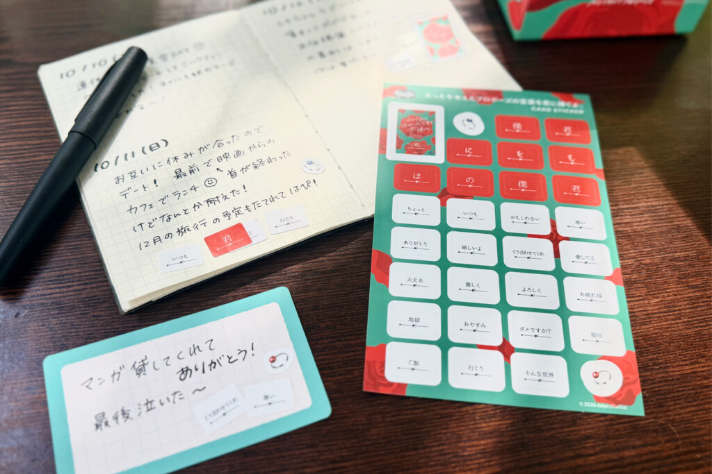赤と白の言葉パーツが並んだSTAMP STICKERのシートと、手帳に貼られたシール